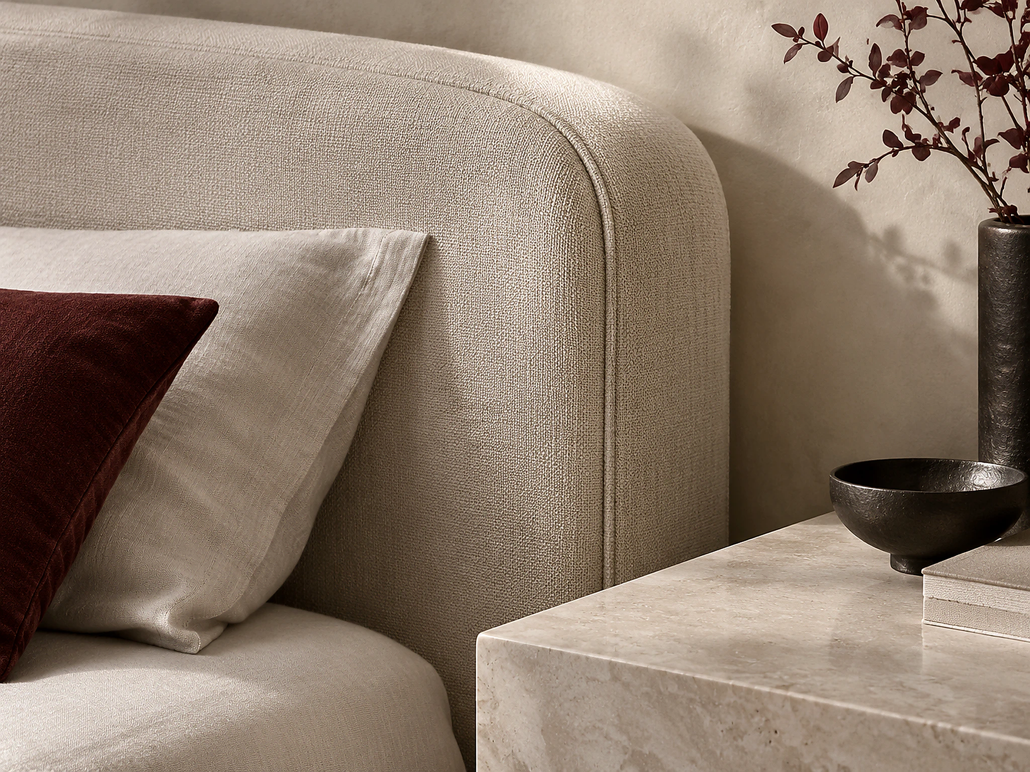 Close view of a curved upholstered headboard, burgundy cushion, and pale bedside surface