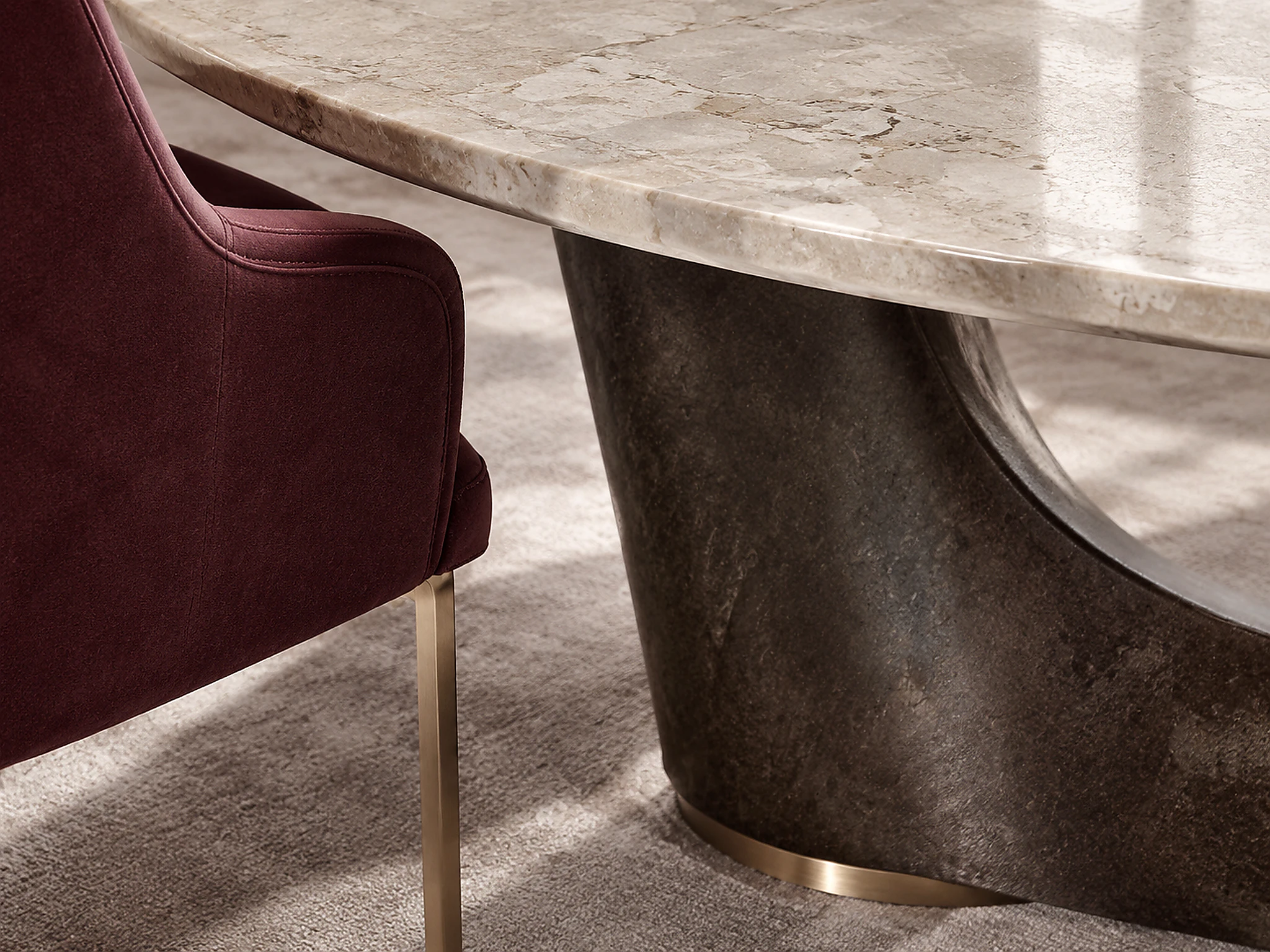 Close view of a mineral dining tabletop, tailored burgundy chair, and sculptural dark base