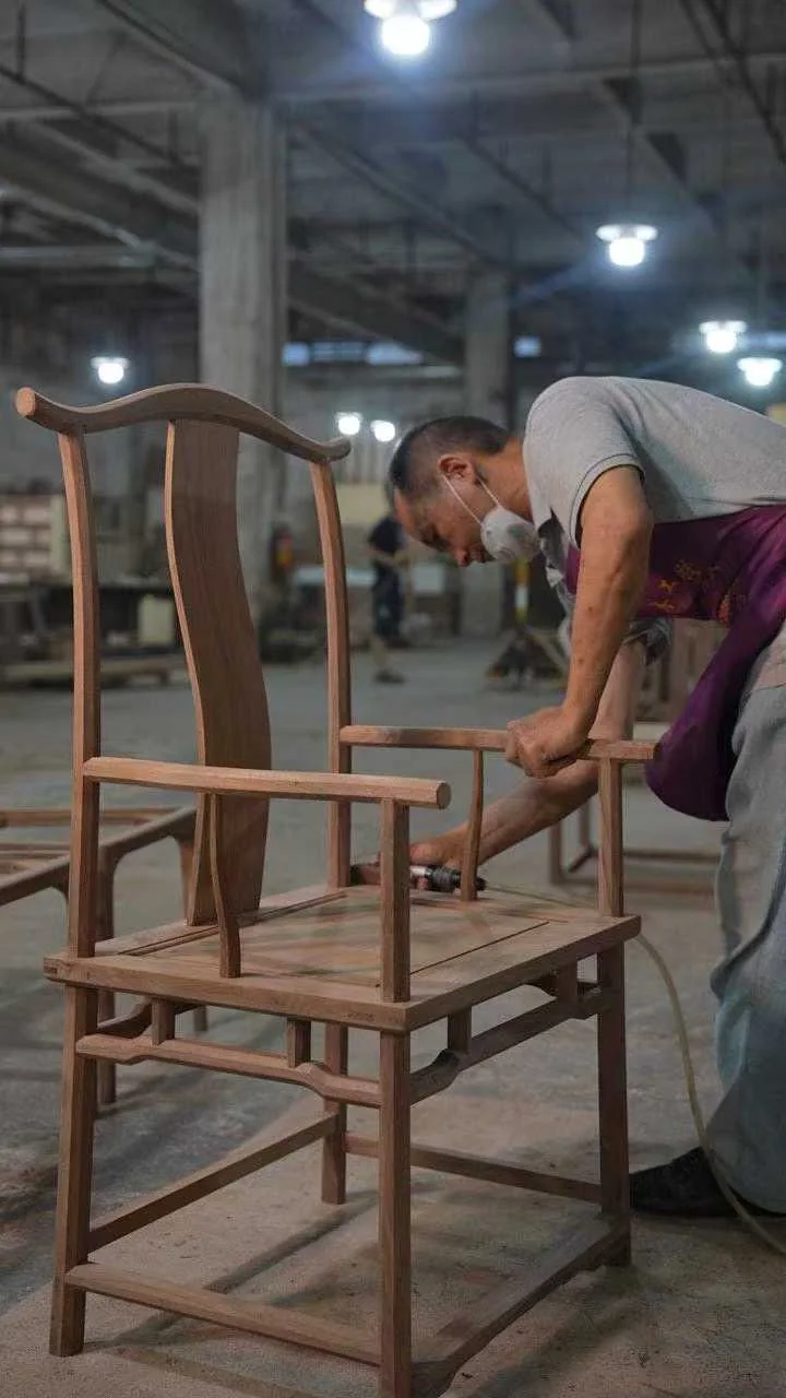 A worker positioning a wooden chair frame at a workshop bench