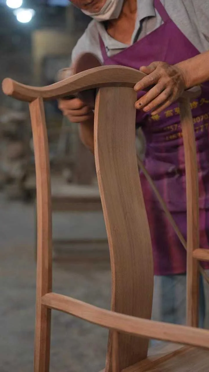 A craftsperson refining the curved rail of a wooden chair
