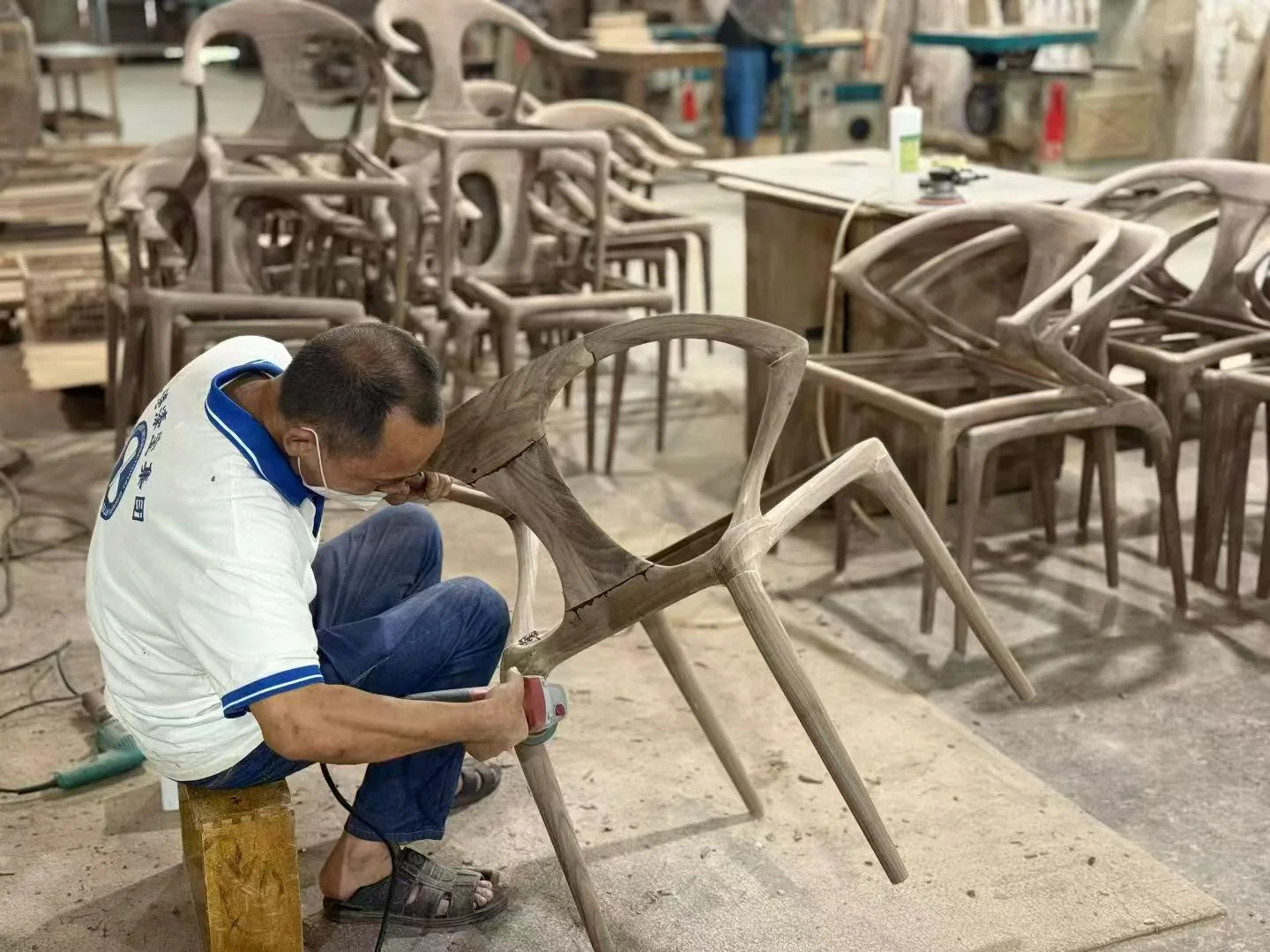 A craftsperson sanding a curved wooden chair frame in a workshop
